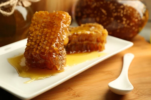 Honeycoms y cuchara en el plato sobre fondo brillante —  Fotos de Stock