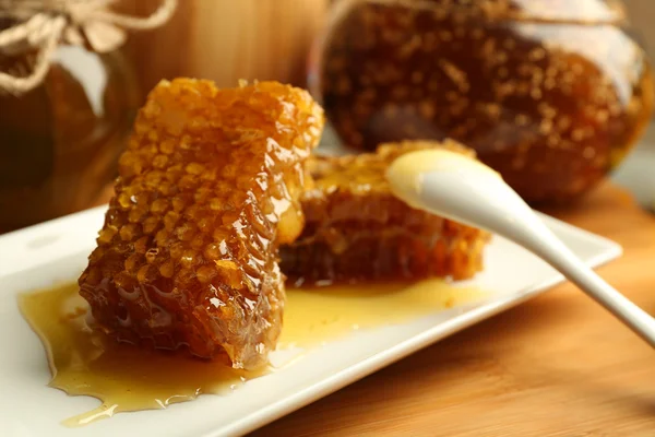 Pentes de mel e colher na placa no fundo brilhante — Fotografia de Stock