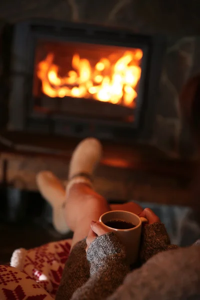 Woman with cup of hot drink near fireplace