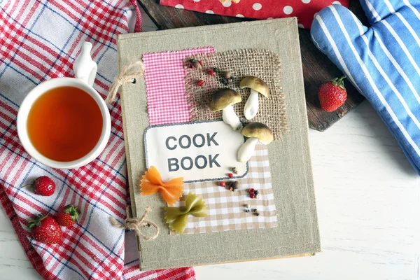 Libro di cucina decorato con tazza di tè e gustosa torta sul tavolo — Foto Stock