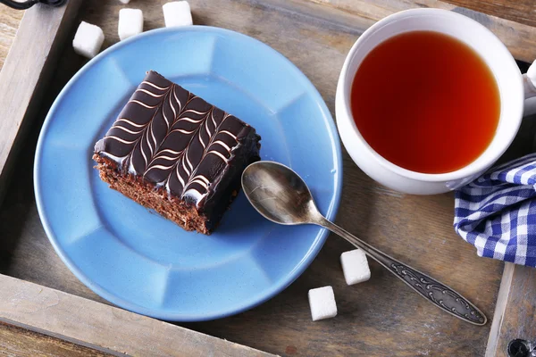 Sweet chocolate cake on blue plate with cup of tea on wooden tray — Stock Photo, Image