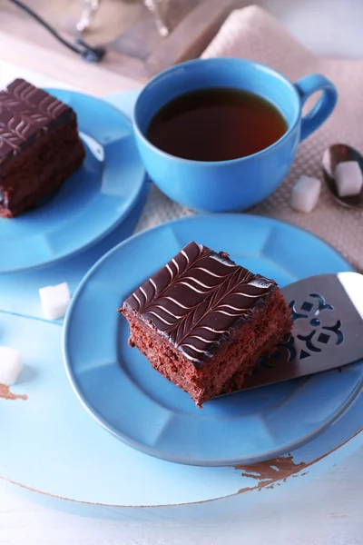 Served table with a cup of tea and chocolate cakes on blue plates close-up — Stock Photo, Image