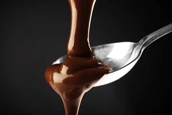Coklat dituangkan pada sendok pada latar belakang gelap — Stok Foto