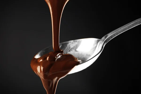 Çikolata koyu arka plan üzerine kaşıkla dökülür — Stok fotoğraf