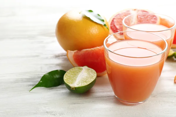 Dois copos de suco cítrico e frutas frescas em fundo de madeira leve — Fotografia de Stock