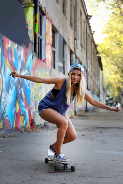 Mujer joven patinando en la tabla de patinaje sobre fondo de pared pintado —  Fotos de Stock
