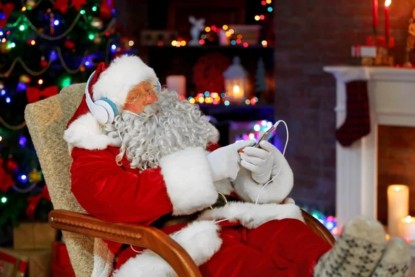 Babbo Natale seduto con le cuffie seduto in comoda sedia a dondolo a casa — Foto Stock