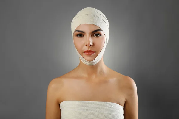 Jovem mulher bonita com uma bandagem elástica na cabeça e no peito, em fundo cinza — Fotografia de Stock
