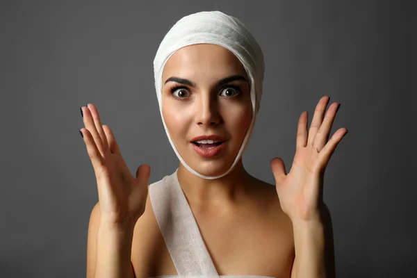 Junge emotionale Frau mit Mullbinde am Kopf, auf grauem Hintergrund — Stockfoto