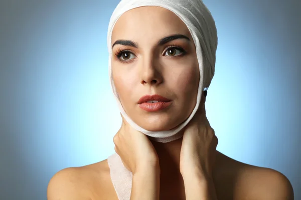 Jovem mulher bonita com uma bandagem de gaze na cabeça, em fundo cinza-azul — Fotografia de Stock