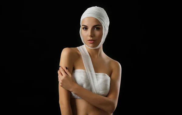 Young beautiful woman with a gauze bandage on her head and chest, on black background — Stock Photo, Image