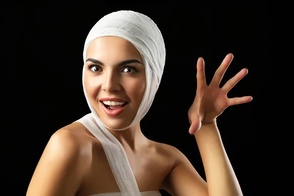Young playful woman with a gauze bandage on her head, on black background — Stok fotoğraf