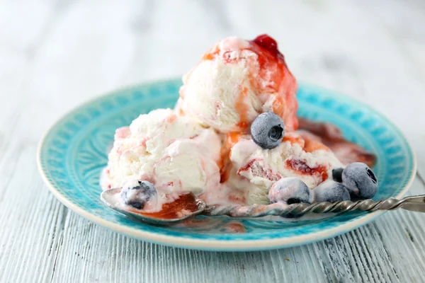 Finom fagylalt friss fagyasztott bogyók és a mártással, színes fából készült háttér — Stock Fotó