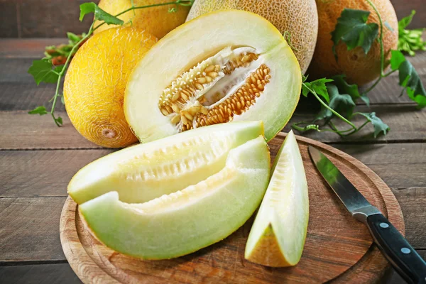 Rijpe meloenen met groene bladeren op houten tafel close-up — Stockfoto