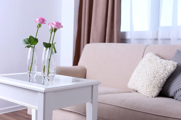 Диван с красивыми подушками и целенаправленной вазой с цветами на столе перед ним в комнате — стоковое фото