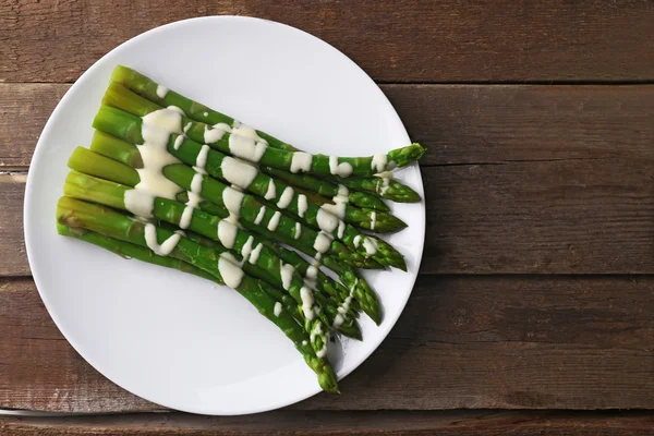 Espárragos apetitosos en salsa de crema agria sobre plato blanco sobre fondo de madera —  Fotos de Stock