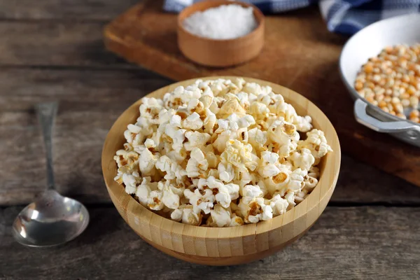 Palomitas saladas en un tazón decorado con utensilios de cocina sobre mesa de madera — Foto de Stock