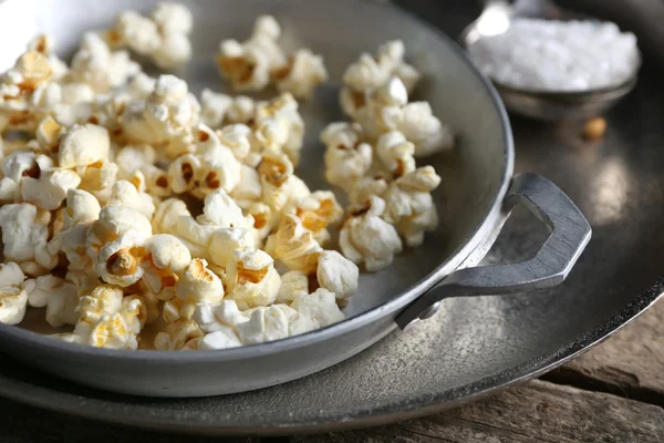 Gezouten popcorn in een metaalkom met kop van likdoorns op houten tafel, close-up — Stockfoto