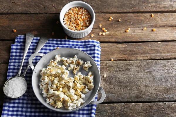 Palomitas saladas en un tazón de metal con taza de callos en una servilleta de algodón a cuadros sobre una mesa de madera —  Fotos de Stock