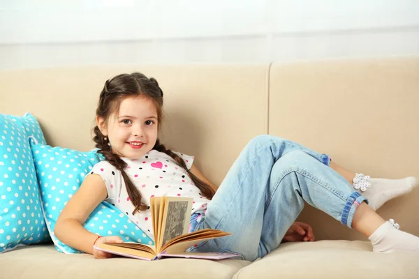 Bambina seduta sul divano con libro — Foto Stock