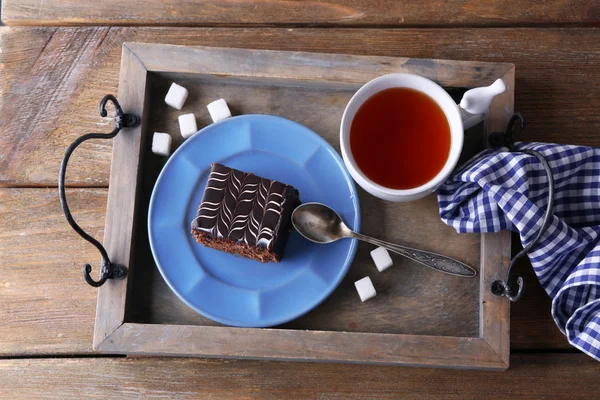 Pastel de chocolate dulce en plato azul con taza de té en bandeja de madera —  Fotos de Stock