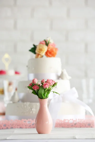 Wedding cake and flowers in vase on decorated table — Stock Photo, Image