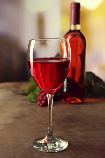 Bicchiere di vino rosso con bottiglia su tavolo di legno su sfondo sfocato — Foto Stock