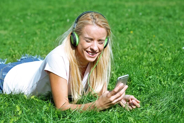 Ung kvinna med hörlurar och lyssna på musik på gräs smartphone — Stockfoto