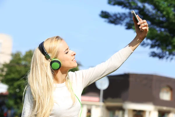 Mujer joven escuchando música y haciendo selfie afuera —  Fotos de Stock