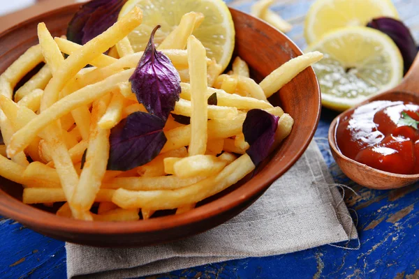 French fried potatoes in bowl with basil and sauce on old wooden background — Stock Photo, Image