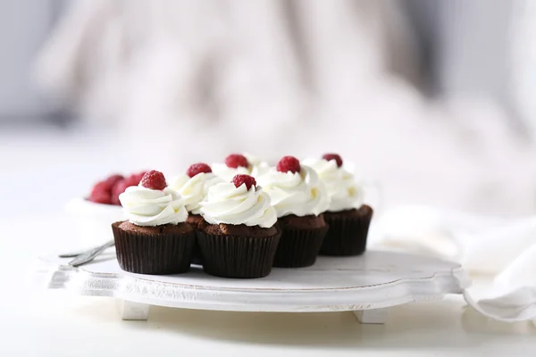 Hermosos cupcakes de chocolate con crema y frambuesa en la mesa — Foto de Stock