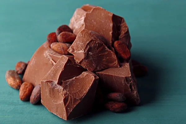 Pedaços de chocolate ao leite e grãos de cacau na cor de fundo de madeira — Fotografia de Stock