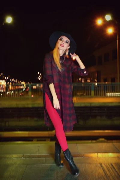 Szczęśliwy stylowe kobieta w kapeluszu pozuje na moście w nocy — Zdjęcie stockowe