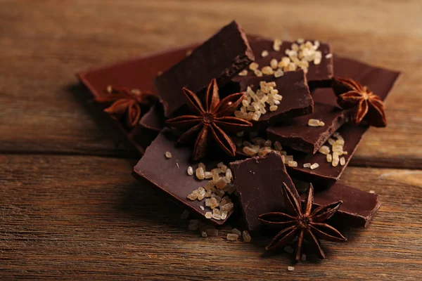 Части черного шоколада со специями на деревянном фоне — стоковое фото
