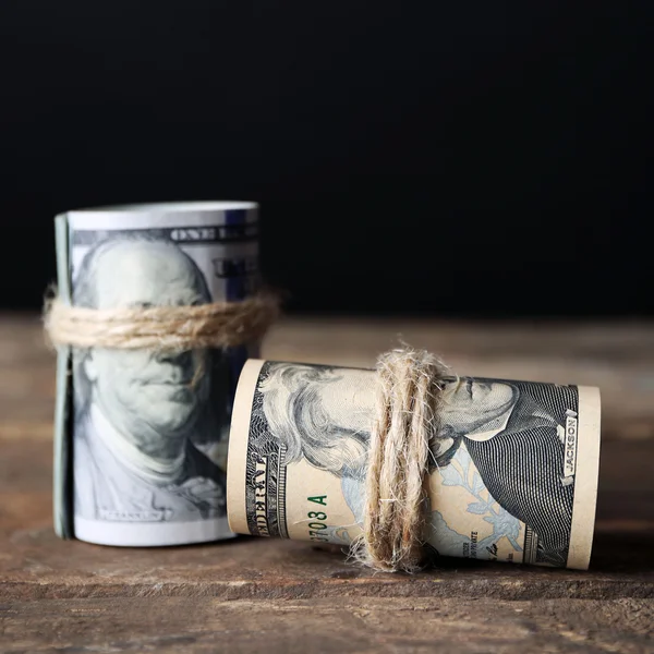 Rollo de dólares sobre mesa de madera delante de fondo oscuro — Foto de Stock