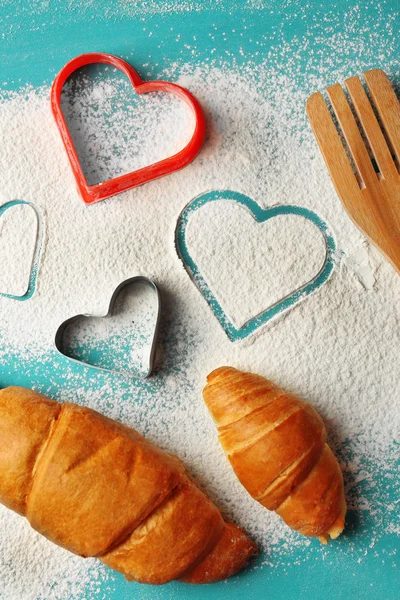 Herz aus Mehl, Croissants auf farbigem Holzhintergrund — Stockfoto