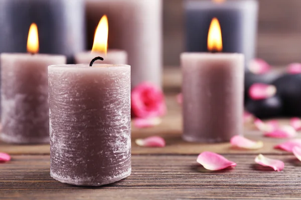 Alight wax grey candle with flower petals and pebbles on wooden background — Stock Photo, Image