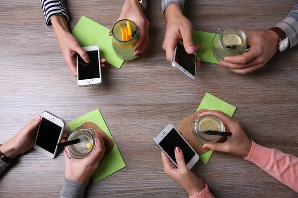 Kokteyller, ahşap masa arka planda tutarak akıllı telefonlar ile dört el — Stok fotoğraf