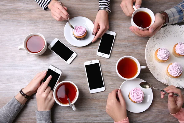 Quatre mains avec téléphones intelligents tenant tasses avec thé, sur fond de table en bois — Photo