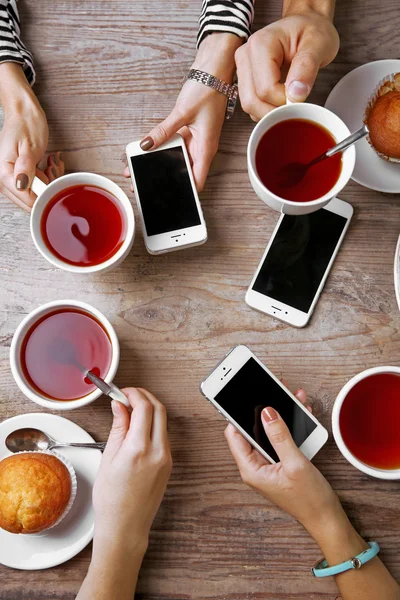 Fyra händer med smarta telefoner hålla koppar med te, på träbord bakgrund — Stockfoto