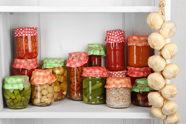 Jars with pickled vegetables and beans on wooden shelf