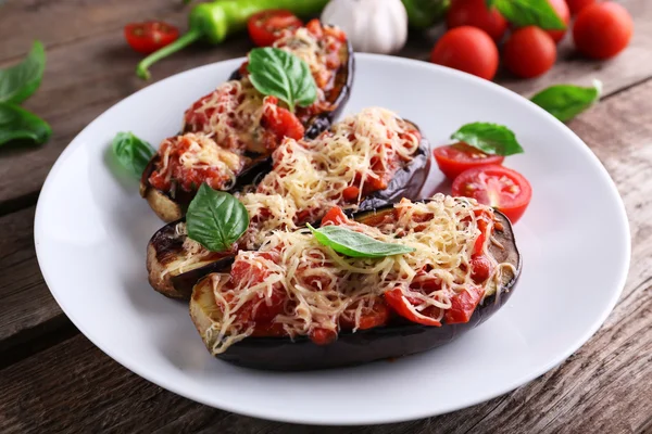 Dish of eggplant with cherry tomatoes and cheese in white plate on wooden table, closeup — Stock Photo, Image