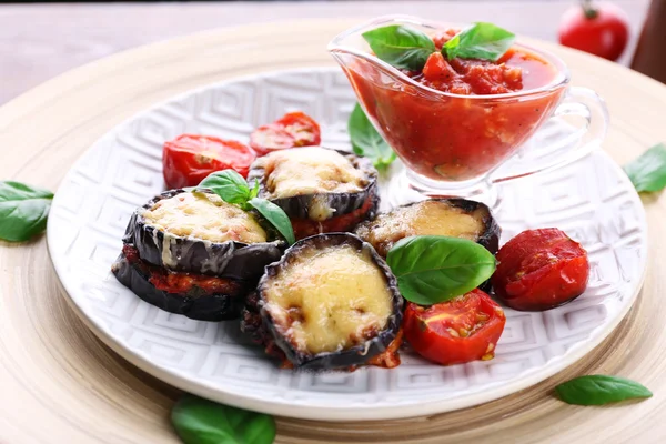 Dish of eggplant with cherry tomatoes and cheese in white plate on wooden table, closeup — Stock Photo, Image