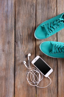 Kulaklık ve lastikbotlar vernikli ahşap arka plan üzerinde beyaz cep telefonu