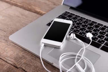 Kulaklıklarla laptop ahşap arka plan üzerinde beyaz cep telefonu