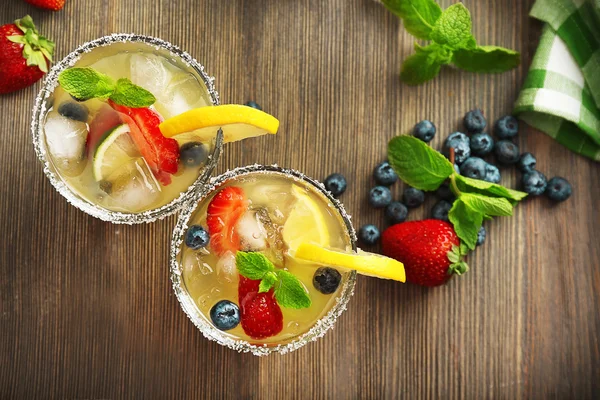 Glasses of berries juice with lemon on wooden table, top view