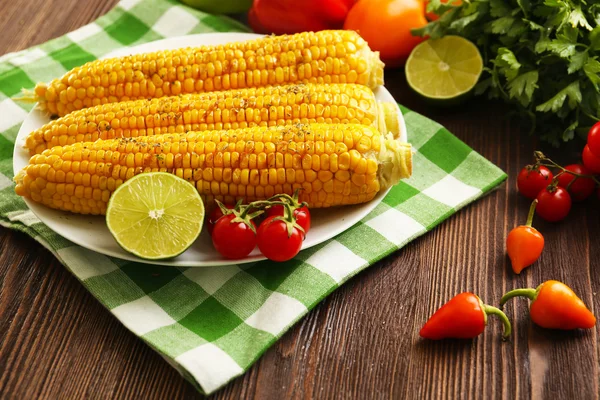 Smakelijk gegrild maïs geserveerd met groenten en groene geruite patroon servet — Stockfoto