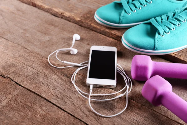 Cellulaire blanc avec écouteurs et cloches muettes roses et gumshoes sur fond en bois — Photo