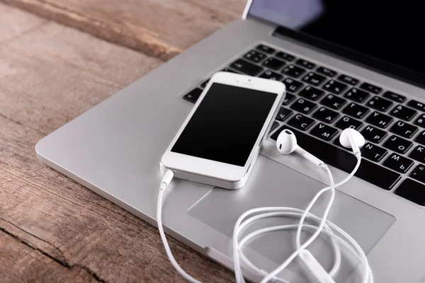 Білий мобільний телефон з навушниками на ноутбуці на дерев'яному фоні — стокове фото