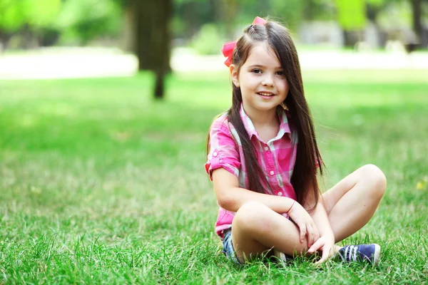 Lycklig liten flicka på det gröna gräset i parken — Stockfoto